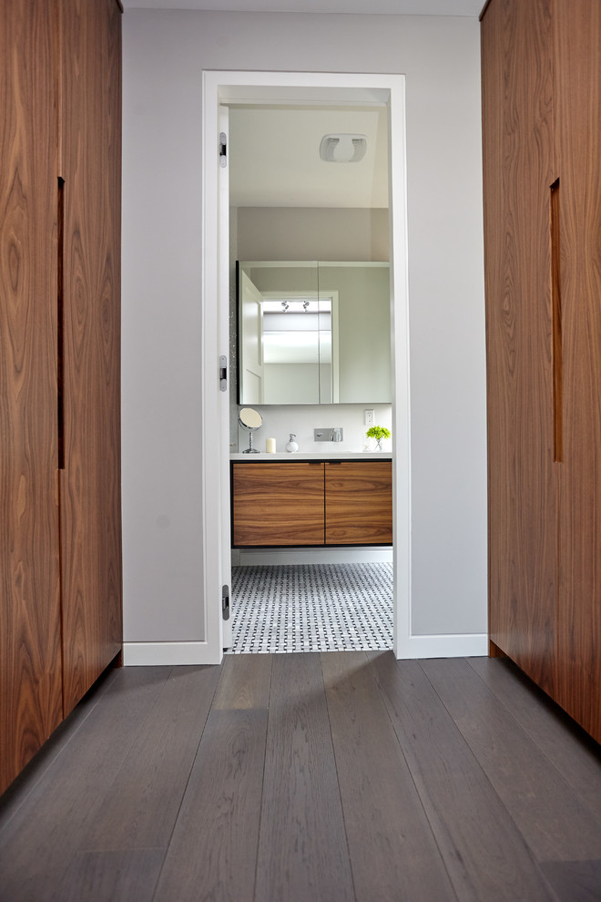 Cette image montre un dressing minimaliste en bois brun de taille moyenne et neutre avec un placard à porte plane, un sol en bois brun et un sol marron.
