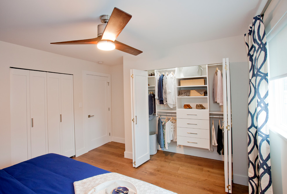 Modelo de armario vestidor clásico renovado de tamaño medio con armarios con paneles lisos, puertas de armario blancas, suelo de madera oscura y suelo marrón