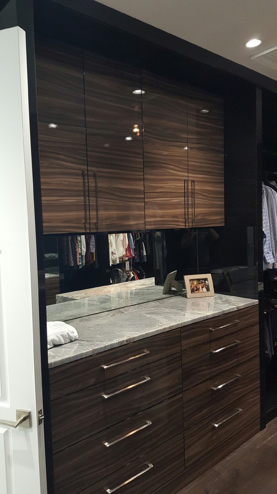Imagen de armario vestidor unisex actual de tamaño medio con armarios con paneles lisos, puertas de armario de madera oscura, suelo de madera en tonos medios y suelo marrón