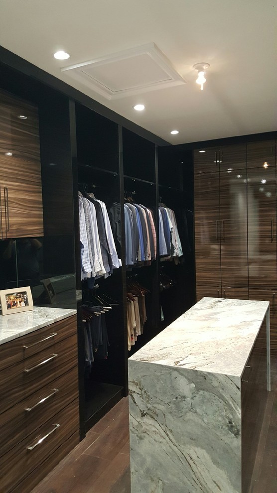 Modelo de armario vestidor unisex actual de tamaño medio con armarios con paneles lisos, puertas de armario de madera oscura, suelo de madera en tonos medios y suelo marrón