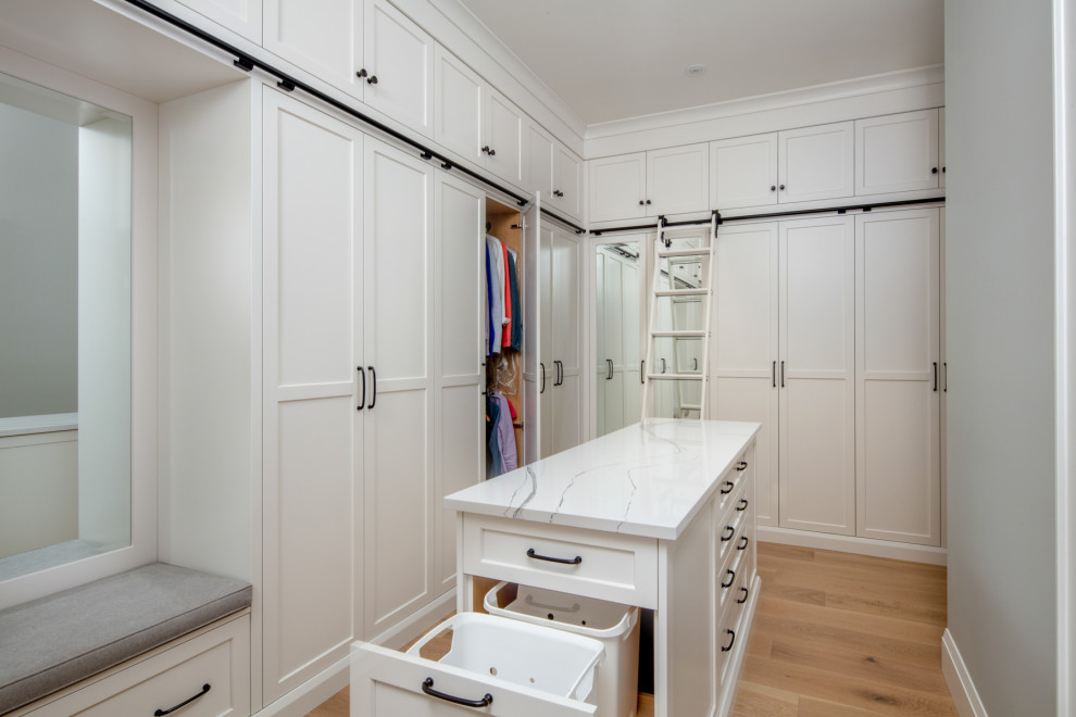 This is an example of an expansive traditional walk-in wardrobe in Toronto with shaker cabinets, white cabinets and light hardwood flooring.