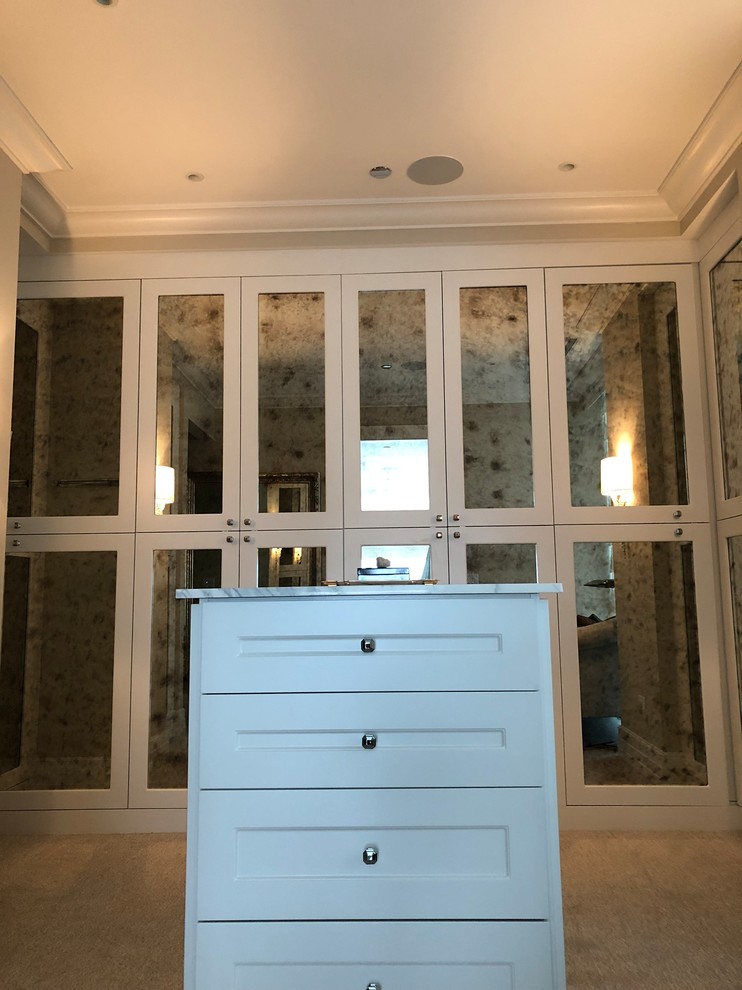 Inspiration for a large classic gender neutral walk-in wardrobe in Chicago with glass-front cabinets, white cabinets, carpet and beige floors.