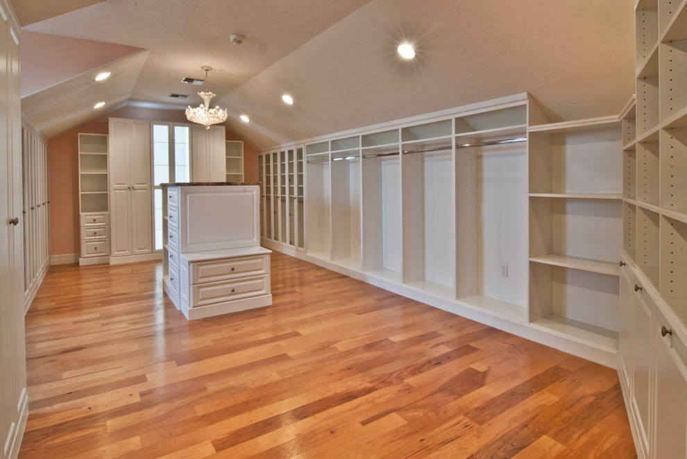 Ejemplo de armario vestidor unisex tradicional grande con armarios con paneles con relieve, puertas de armario blancas y suelo de madera en tonos medios