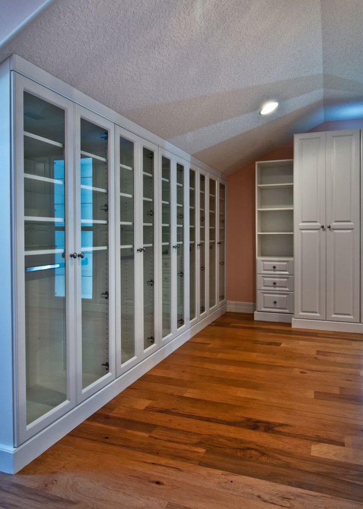 Cette photo montre un grand dressing tendance neutre avec un placard avec porte à panneau surélevé, des portes de placard blanches et un sol en bois brun.