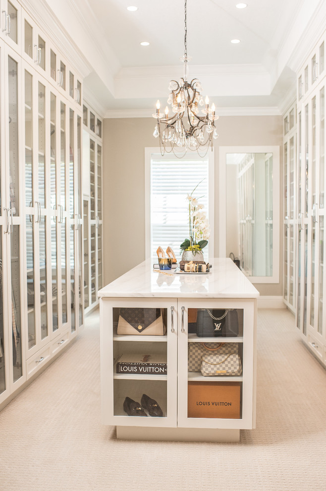 Inspiration for a large traditional gender neutral walk-in wardrobe in Orlando with glass-front cabinets, white cabinets, carpet and beige floors.
