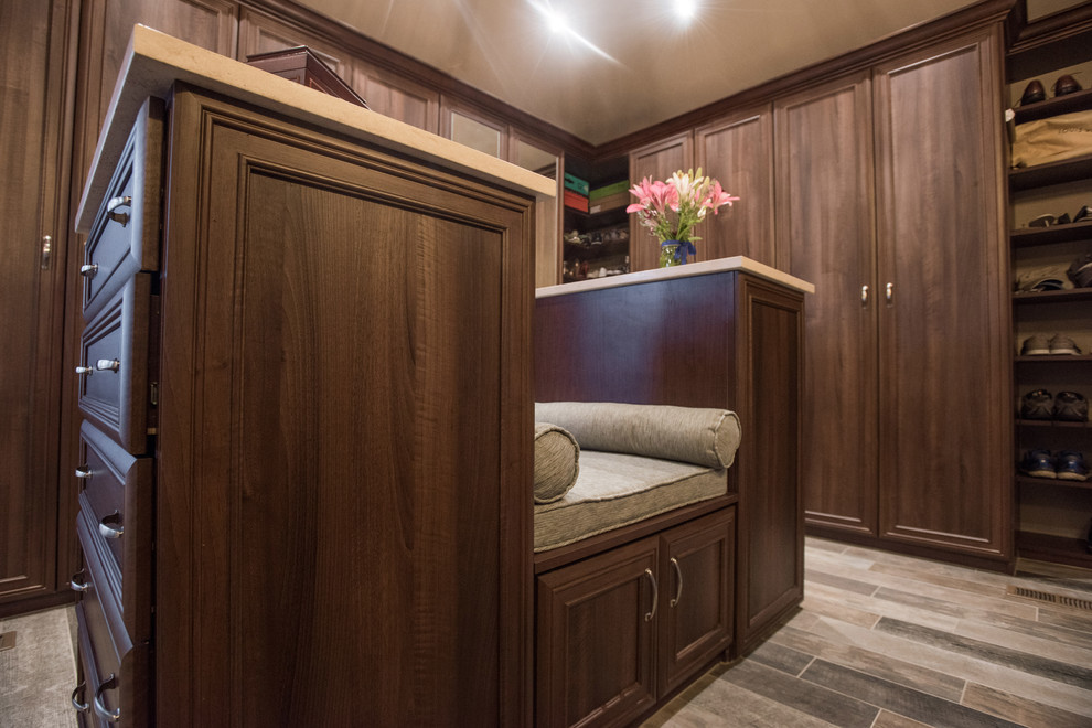 デンバーにある広いトランジショナルスタイルのおしゃれなウォークインクローゼット (落し込みパネル扉のキャビネット、中間色木目調キャビネット、ライムストーンの床、グレーの床) の写真