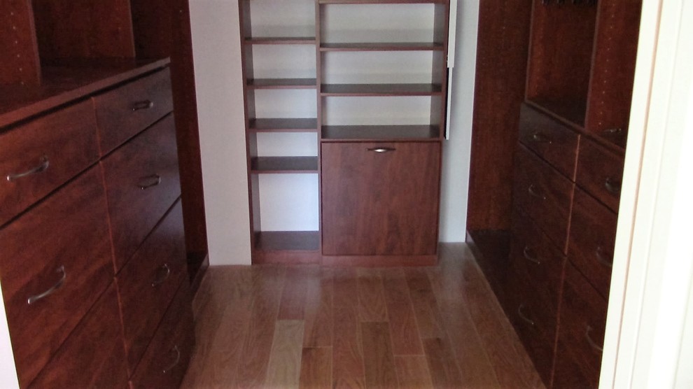 Immagine di una cabina armadio unisex classica di medie dimensioni con ante in legno scuro, ante lisce, pavimento in legno massello medio e pavimento marrone