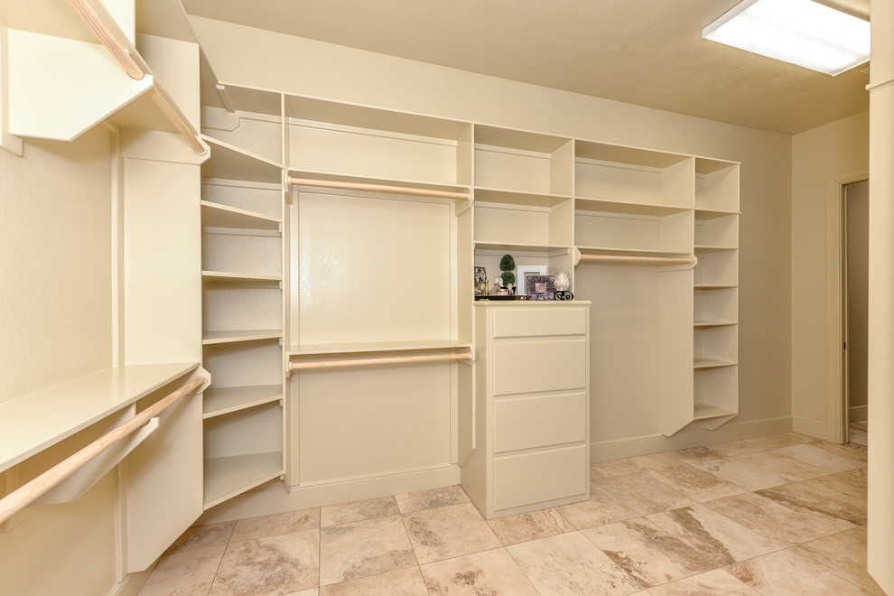 Large mountain style gender-neutral travertine floor walk-in closet photo in Austin with open cabinets and beige cabinets