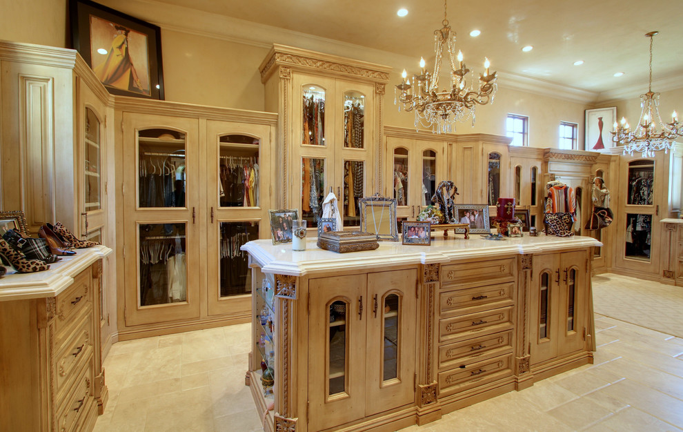 Inspiration for an expansive traditional dressing room for women in Phoenix with glass-front cabinets, medium wood cabinets and travertine flooring.