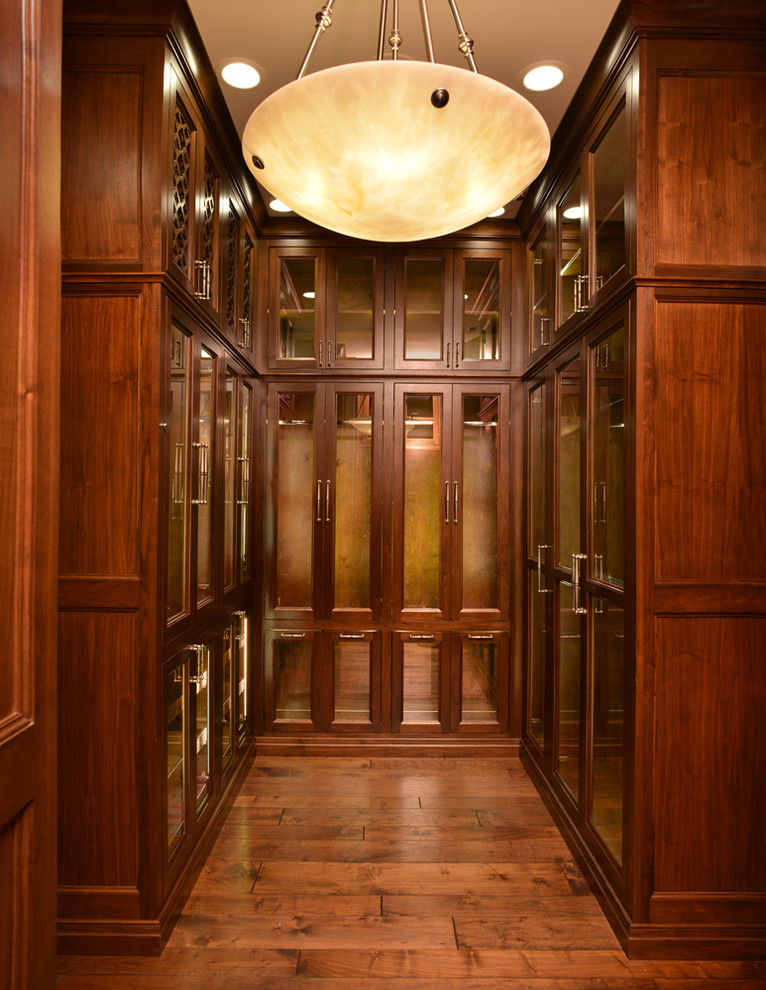 Imagen de vestidor de hombre clásico renovado grande con armarios tipo vitrina, puertas de armario de madera oscura y suelo de madera en tonos medios