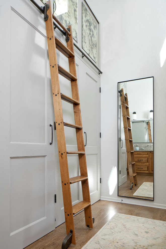 Cette image montre un grand dressing room traditionnel avec un placard avec porte à panneau encastré, des portes de placard blanches et un sol en bois brun.