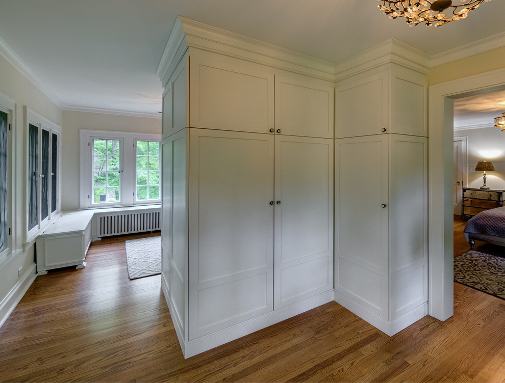 Diseño de vestidor unisex romántico con armarios estilo shaker, puertas de armario blancas y suelo de madera en tonos medios