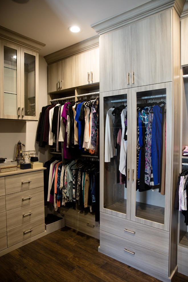 Modelo de armario vestidor de mujer actual grande con armarios con paneles lisos, puertas de armario grises, suelo de madera oscura y suelo marrón