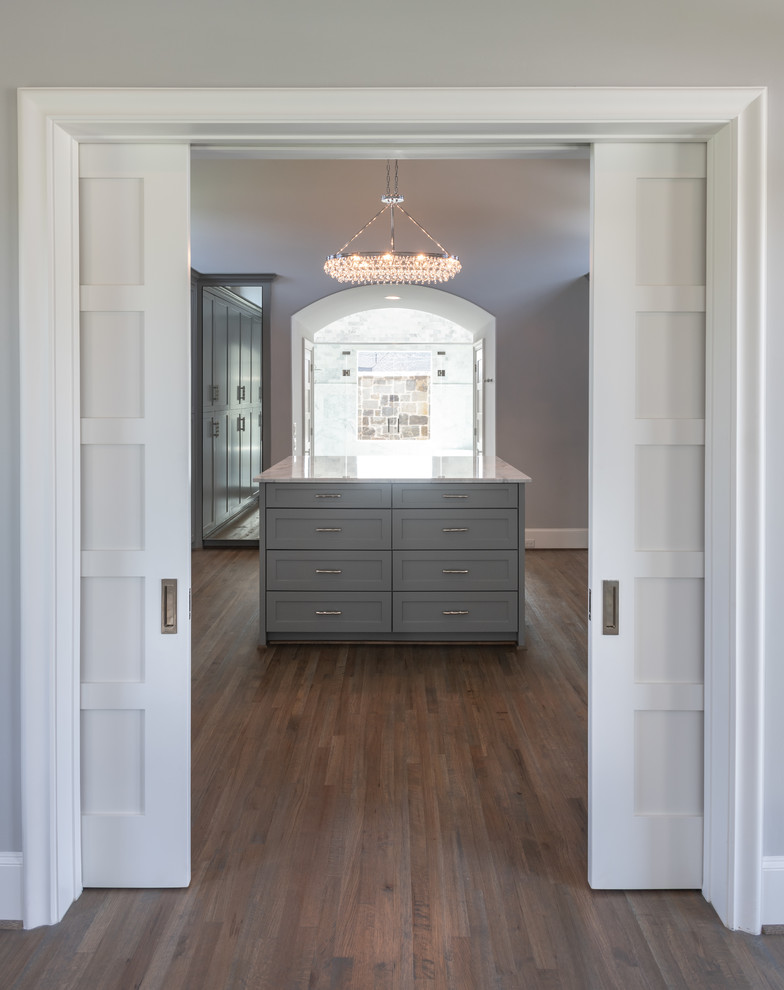 Ejemplo de vestidor unisex clásico renovado grande con armarios estilo shaker, puertas de armario grises, suelo de madera en tonos medios y suelo marrón