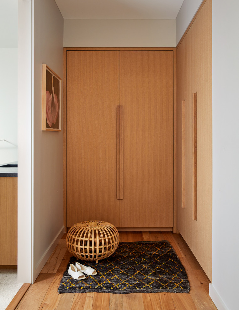 На фото: гардеробная унисекс в скандинавском стиле с плоскими фасадами, светлыми деревянными фасадами и светлым паркетным полом