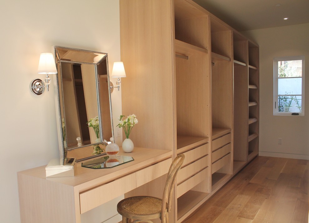 Diseño de armario vestidor unisex mediterráneo de tamaño medio con armarios con paneles lisos, puertas de armario de madera clara y suelo de madera clara