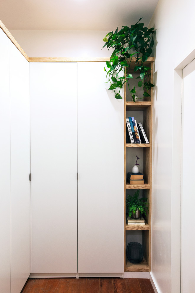 Modelo de vestidor unisex actual pequeño con armarios con paneles lisos, puertas de armario blancas, suelo de madera oscura y suelo multicolor