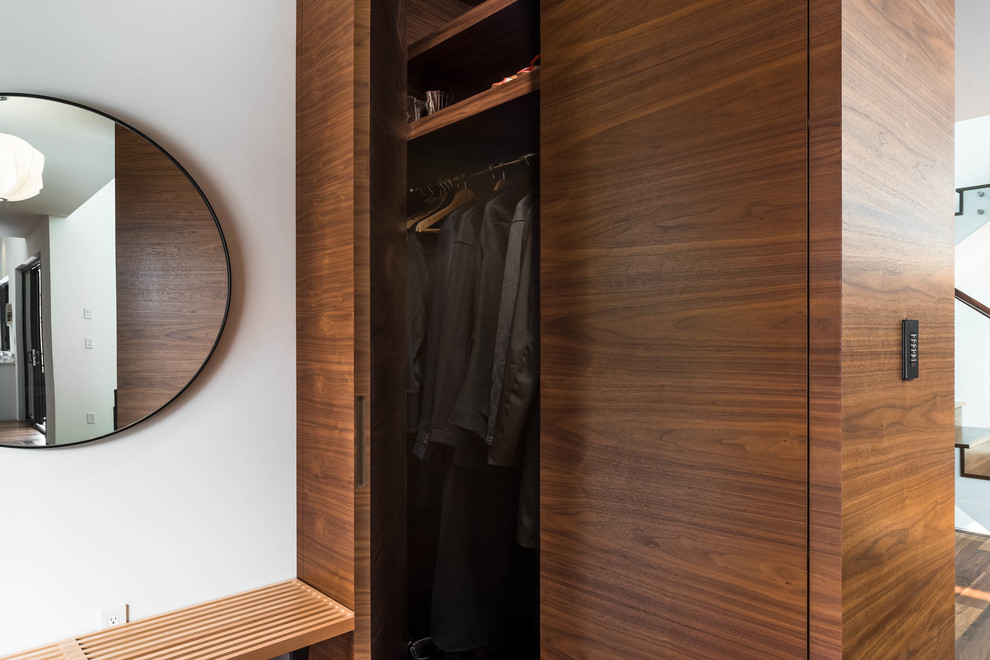 Immagine di un piccolo armadio o armadio a muro unisex minimalista con ante lisce, ante in legno scuro, pavimento in legno massello medio e pavimento marrone
