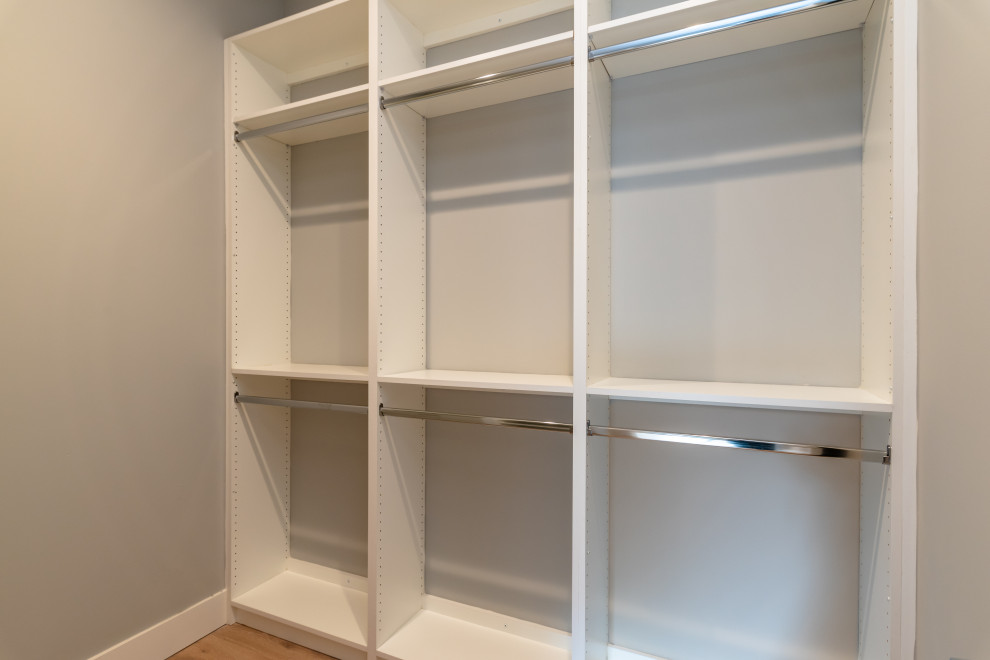 Modelo de armario vestidor unisex minimalista grande con armarios con paneles lisos, puertas de armario blancas, suelo de madera clara y suelo blanco