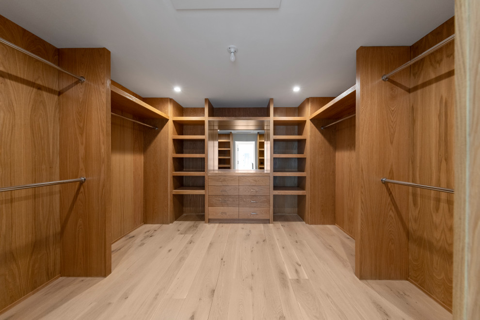 Diseño de armario vestidor unisex contemporáneo grande con armarios con paneles lisos, puertas de armario de madera clara, suelo de madera clara y suelo marrón