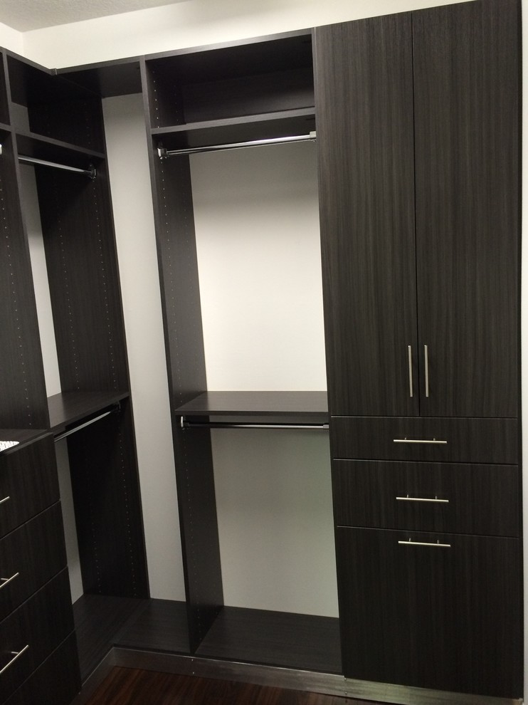Foto de armario vestidor minimalista pequeño con armarios con paneles lisos, puertas de armario grises, suelo de madera oscura y suelo marrón