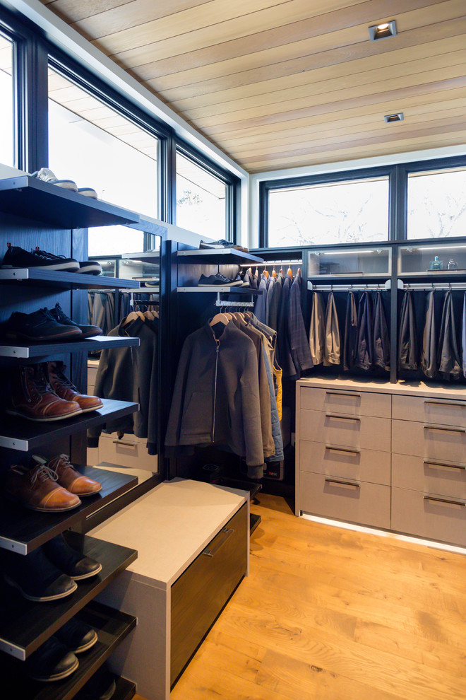 Modelo de vestidor de mujer minimalista grande con armarios con paneles lisos, puertas de armario de madera clara y suelo de madera en tonos medios