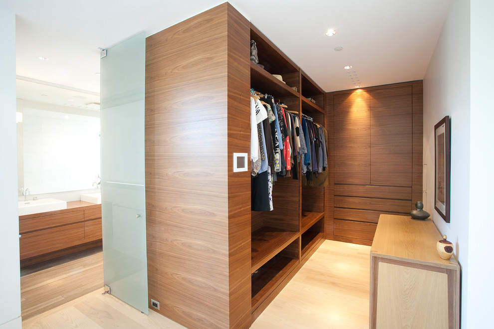 Ejemplo de vestidor unisex moderno de tamaño medio con armarios con paneles lisos, puertas de armario de madera oscura y suelo de madera clara
