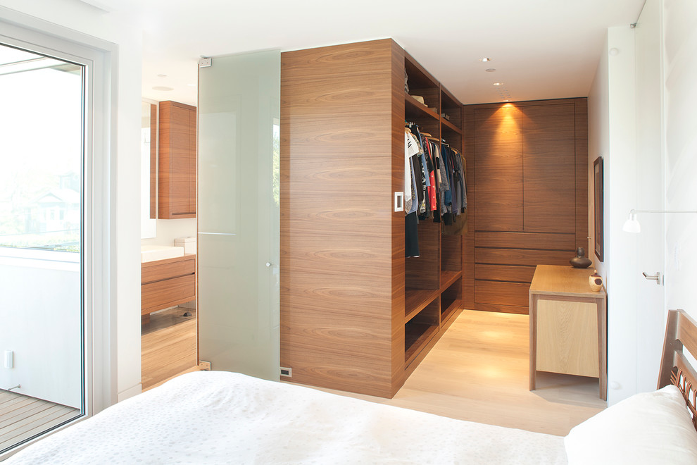 Diseño de vestidor unisex minimalista de tamaño medio con armarios con paneles lisos, puertas de armario de madera oscura y suelo de madera clara