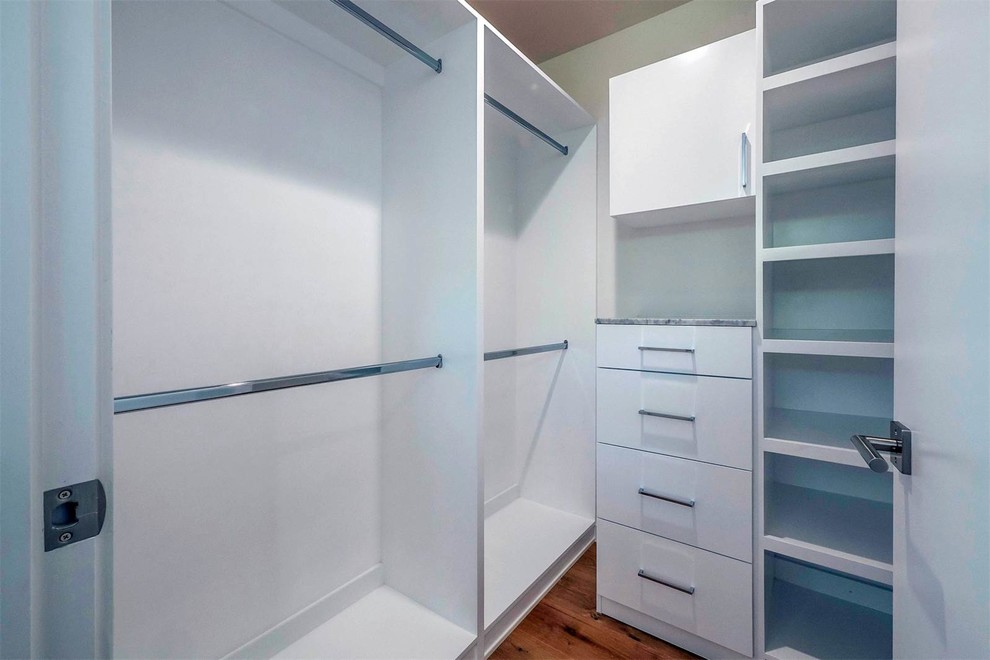 Modelo de armario vestidor unisex minimalista de tamaño medio con armarios con paneles lisos, puertas de armario blancas, suelo de madera en tonos medios y suelo marrón