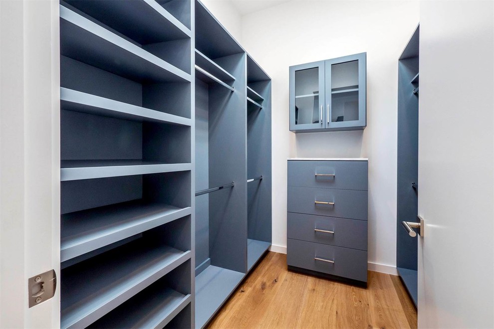 Diseño de armario vestidor unisex minimalista de tamaño medio con armarios con paneles lisos, puertas de armario grises, suelo de madera en tonos medios y suelo marrón