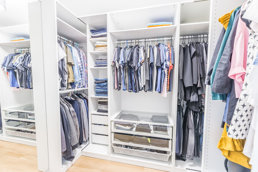 Diseño de armario vestidor unisex minimalista de tamaño medio con armarios abiertos, puertas de armario blancas, suelo de madera clara y suelo marrón