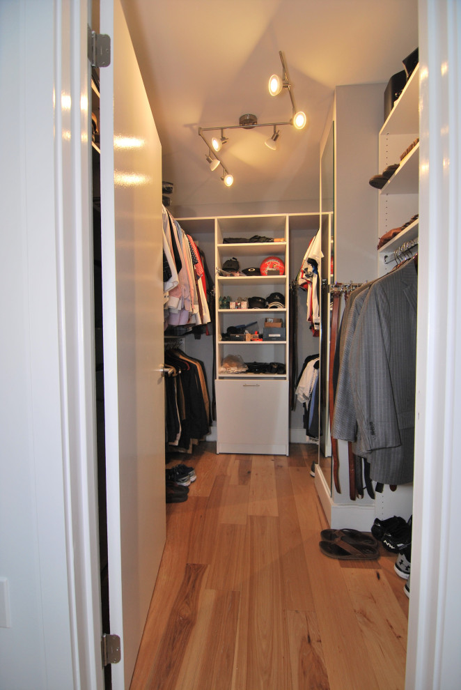 Ejemplo de armario vestidor de hombre moderno pequeño con armarios con paneles lisos, puertas de armario blancas, suelo de madera en tonos medios y suelo multicolor