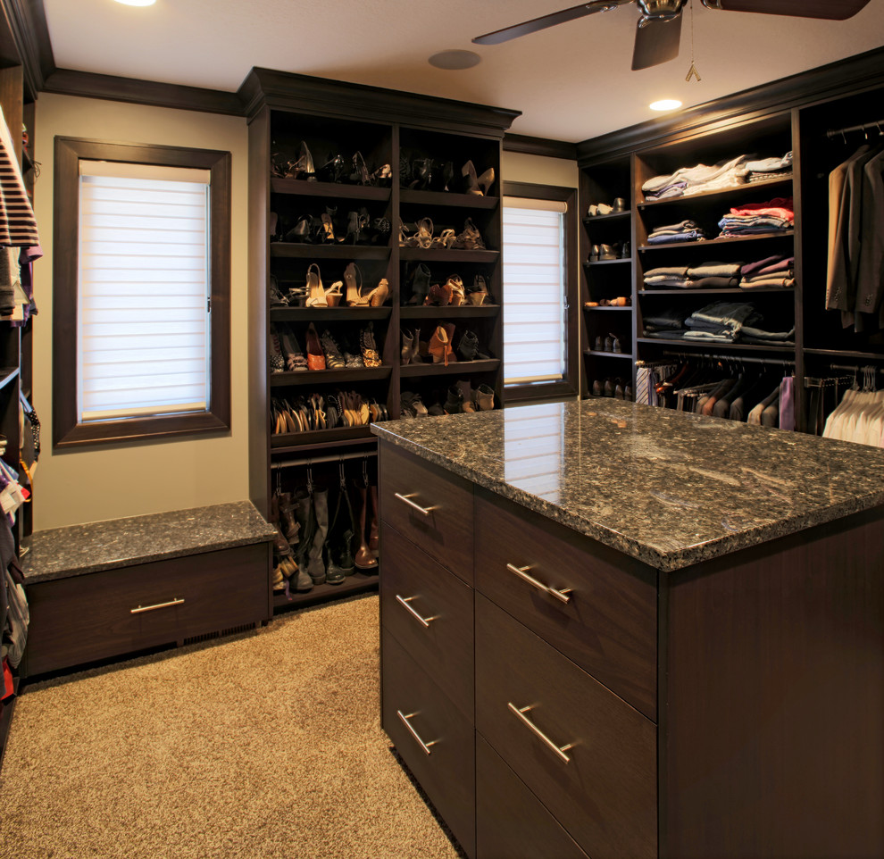 Inspiration for a large classic gender neutral walk-in wardrobe in Kansas City with flat-panel cabinets, dark wood cabinets and carpet.