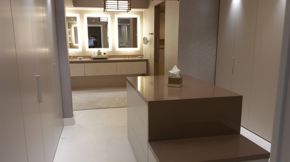 Cette photo montre un grand dressing room moderne neutre avec un placard à porte plane, des portes de placard beiges et un sol en calcaire.