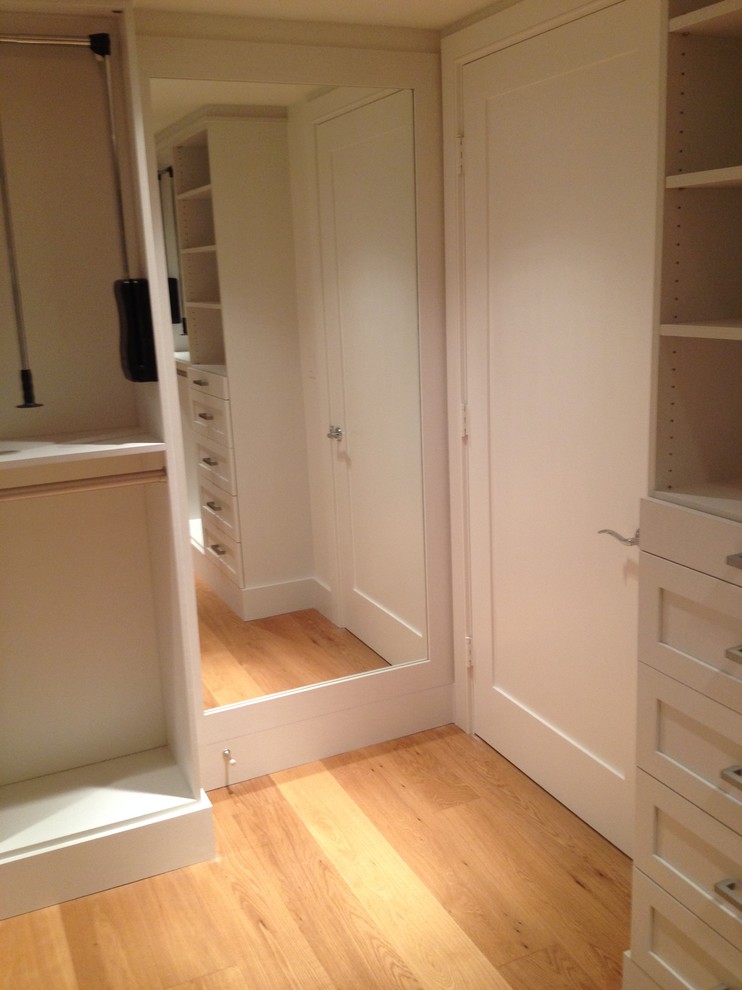 Diseño de armario vestidor unisex clásico grande con armarios estilo shaker, puertas de armario blancas y suelo de madera clara