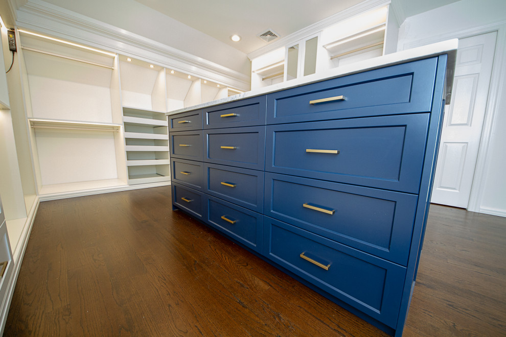 Imagen de armario vestidor unisex tradicional grande con armarios con paneles empotrados, puertas de armario azules y suelo de madera oscura