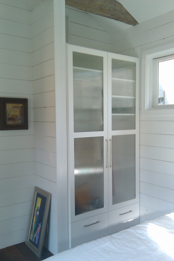 他の地域にある低価格の小さなコンテンポラリースタイルのおしゃれな壁面クローゼット (ガラス扉のキャビネット、白いキャビネット、濃色無垢フローリング) の写真