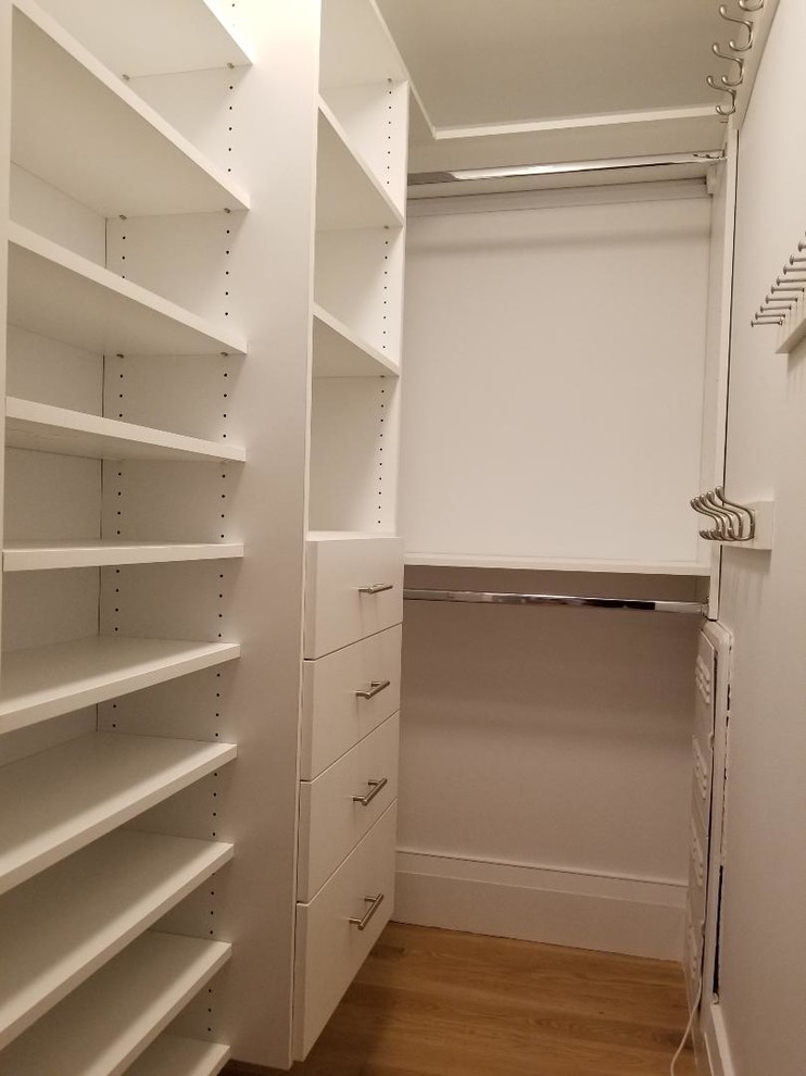 Modelo de armario vestidor unisex actual pequeño con armarios con paneles lisos, puertas de armario blancas, suelo de madera en tonos medios y suelo marrón
