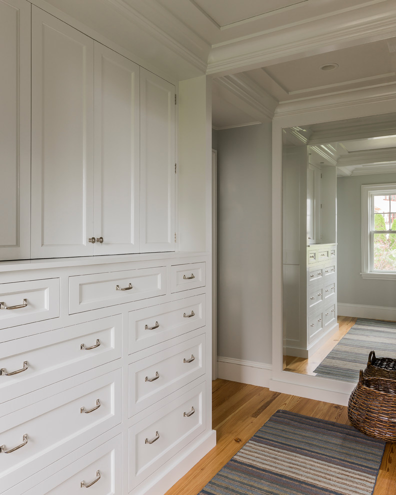 Inspiration for a beach style wardrobe in Boston with white cabinets and medium hardwood flooring.