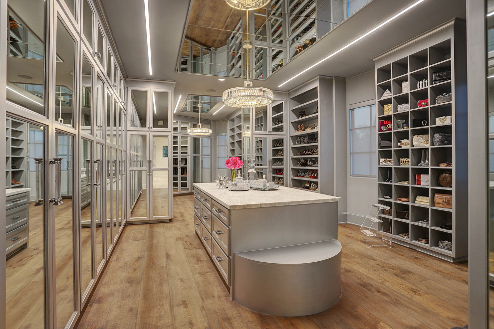 This is an example of a large mediterranean dressing room for women in Houston with recessed-panel cabinets, grey cabinets, light hardwood flooring and beige floors.