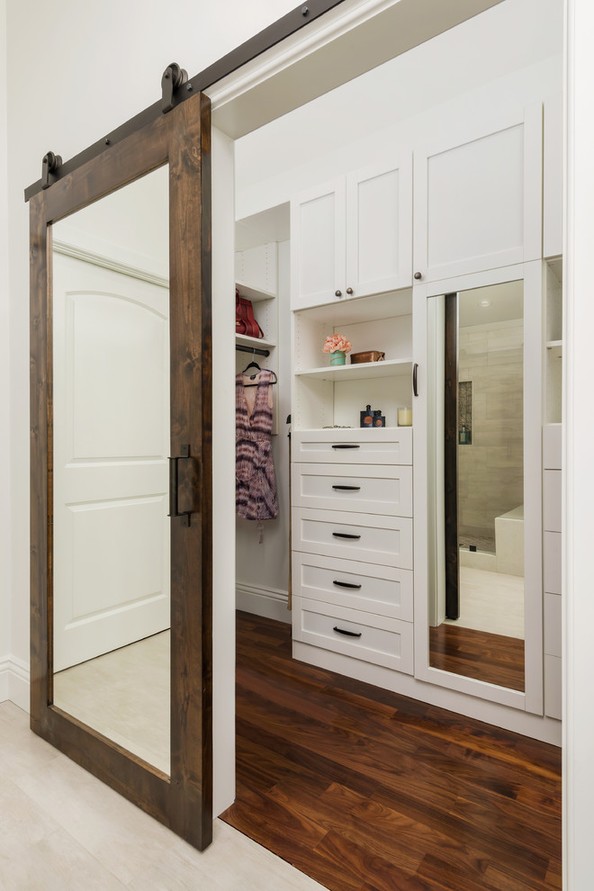 Cette image montre un grand dressing room traditionnel neutre avec un placard à porte shaker, des portes de placard blanches, un sol en bois brun et un sol marron.