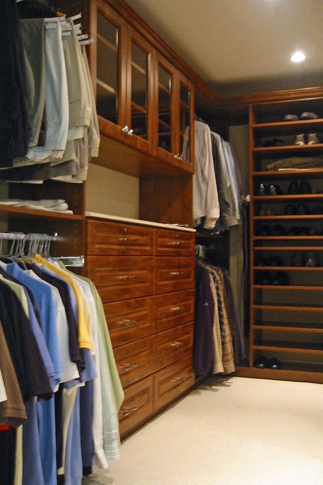 Diseño de armario vestidor de hombre clásico grande con armarios con paneles con relieve, puertas de armario de madera oscura, moqueta y suelo beige