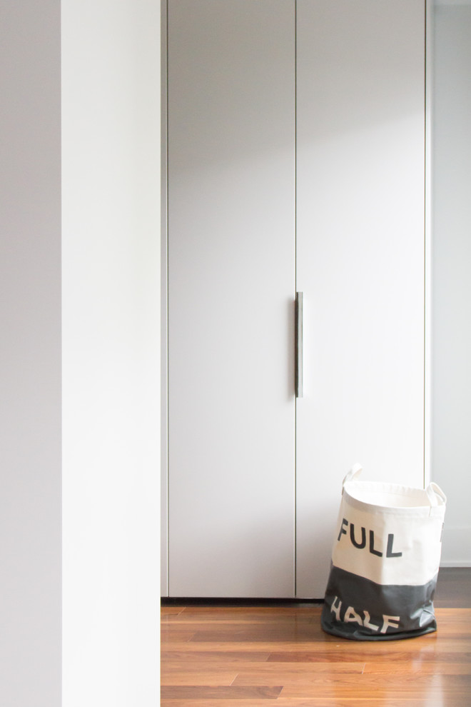 Idées déco pour un dressing room moderne de taille moyenne et neutre avec un placard à porte plane, des portes de placard blanches et un sol en bois brun.