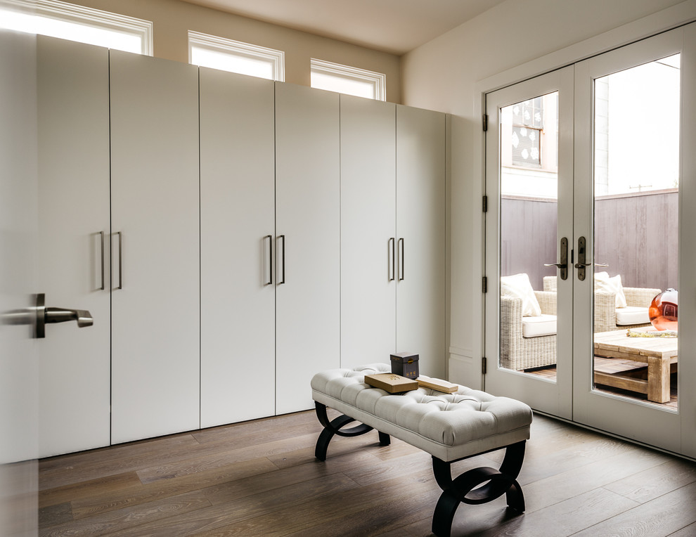 Idée de décoration pour un dressing room design neutre avec un placard à porte plane, des portes de placard blanches, parquet foncé et un sol marron.