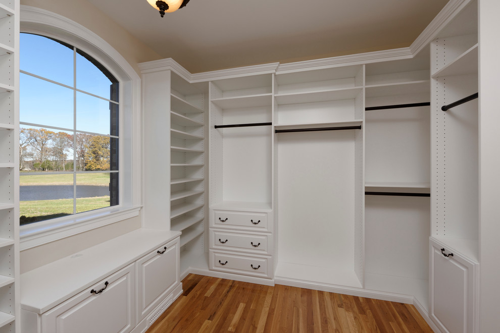 Diseño de vestidor unisex de estilo de casa de campo extra grande con armarios con paneles con relieve, puertas de armario blancas y suelo de madera en tonos medios