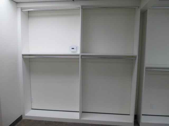 Cette photo montre un grand dressing room moderne neutre avec un placard à porte plane, des portes de placard blanches, sol en béton ciré et un sol gris.
