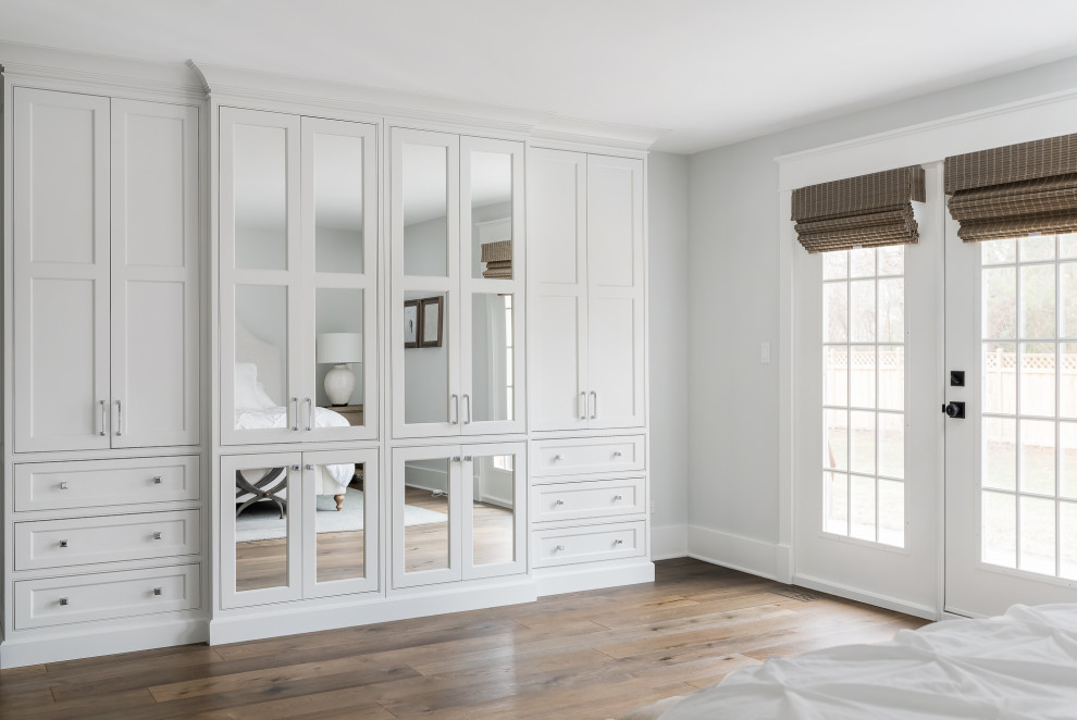 Cette photo montre une armoire encastrée nature de taille moyenne et neutre avec un placard à porte plane, des portes de placard blanches, un sol en bois brun et un sol marron.