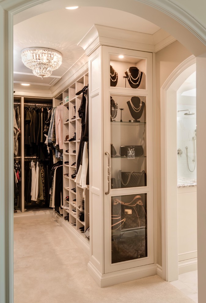 Example of a mid-sized classic women's carpeted and beige floor walk-in closet design in Detroit with glass-front cabinets and light wood cabinets