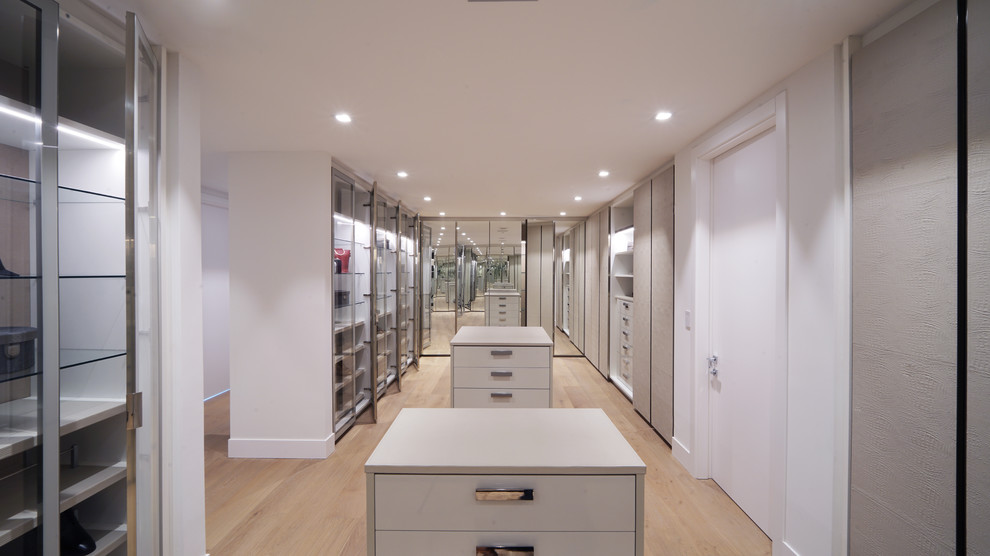 Inspiration for an expansive modern gender neutral walk-in wardrobe in Miami with glass-front cabinets, white cabinets, light hardwood flooring and beige floors.