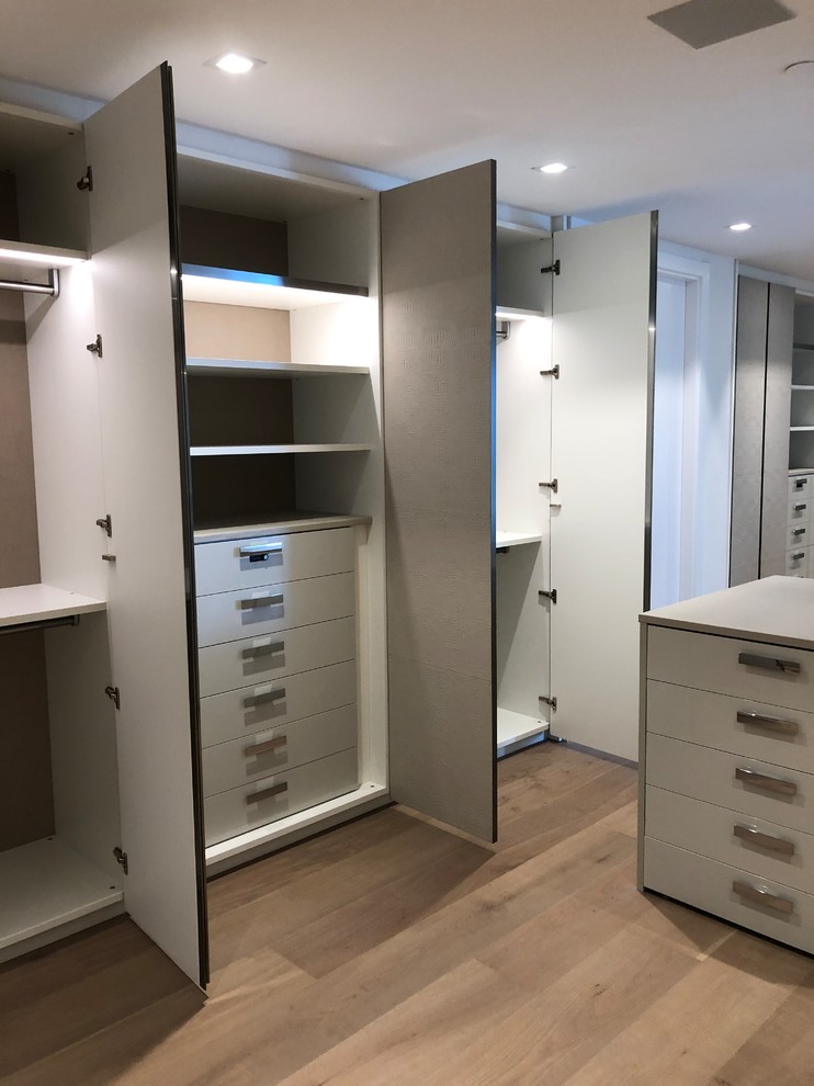 Idee per un'ampia cabina armadio unisex minimalista con ante di vetro, ante bianche, parquet chiaro e pavimento beige